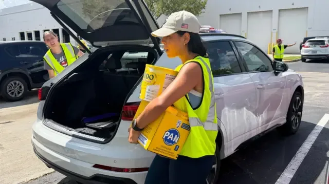Una mujer descarga de un auto una caja de harina de maíz y una lata de leche en polvo, en el centro de donación de Global Empowerment Mission, el 25 de junio de 2025 en Doral, Florida.