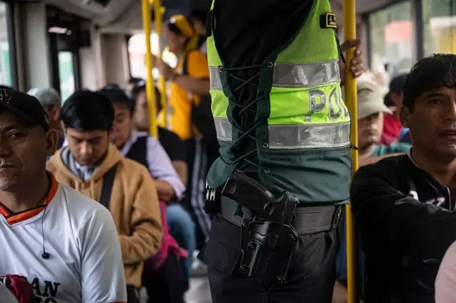 Un policía viaja con su arma reglamentaria en la cintura junto a varias personas sentadas en un autobús en las afueras de Lima, Perú, en abril de 2026
